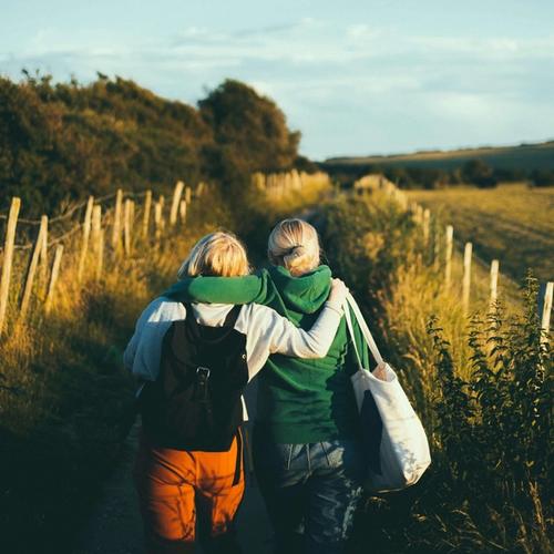 Två kvinnor går på en landsväg med armarna om varandras axel