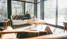 Stue med store vinduer. i sofaen sitter en dame og leser. bilde.