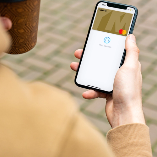 En man håller en take away kaffe och mobil med Apple Pay