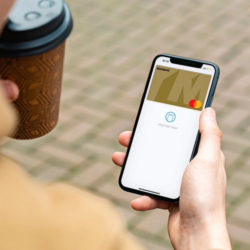 En man håller en take away kaffe och mobil med Apple Pay