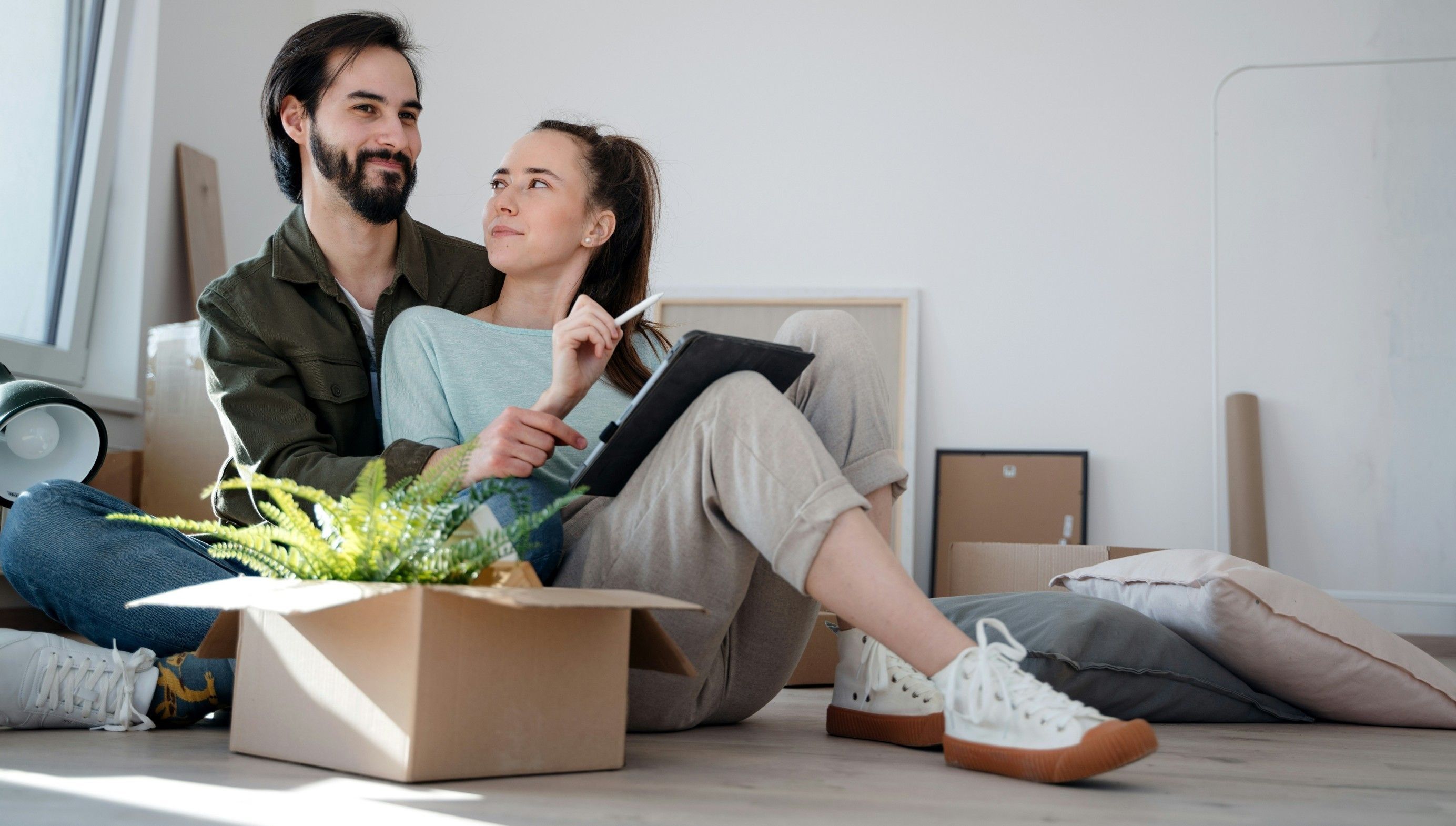 Pariskunta istuu lattialla ja suunnittelee remonttia paperin ja kynän avulla. Valokuva.