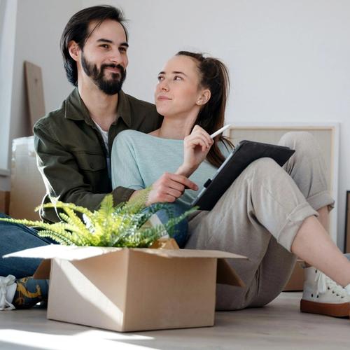 Pariskunta istuu lattialla ja suunnittelee remonttia paperin ja kynän avulla. Valokuva.