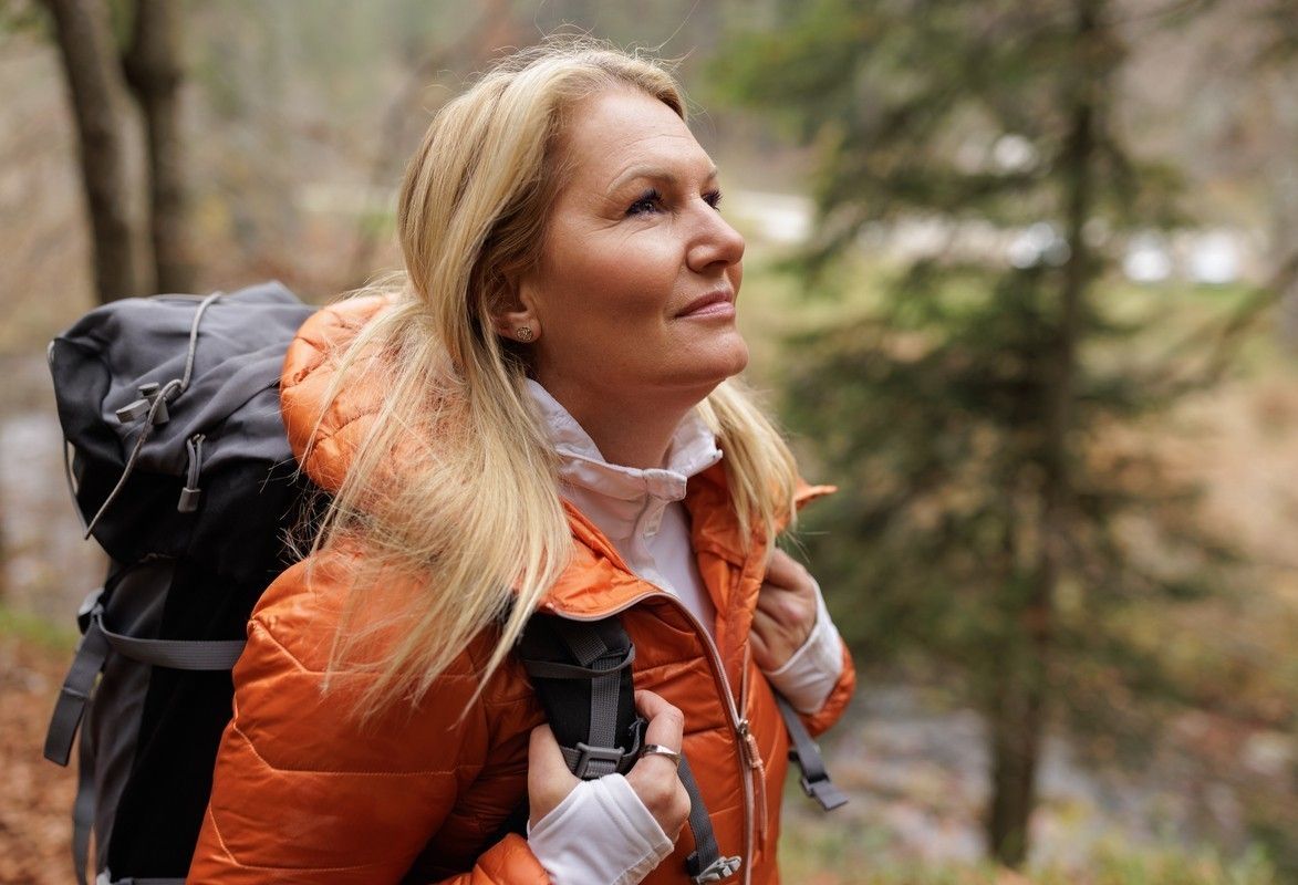 En kvinna med orange jacka och ryggsäck på tur i skogen. foto.