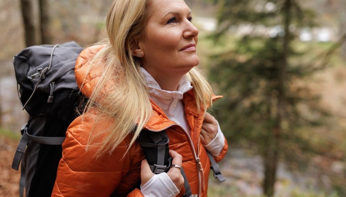 En kvinna med orange jacka och ryggsäck på tur i skogen. foto.