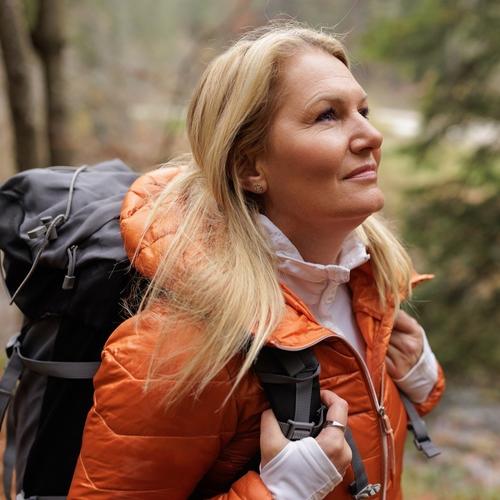 En kvinna med orange jacka och ryggsäck på tur i skogen. foto.