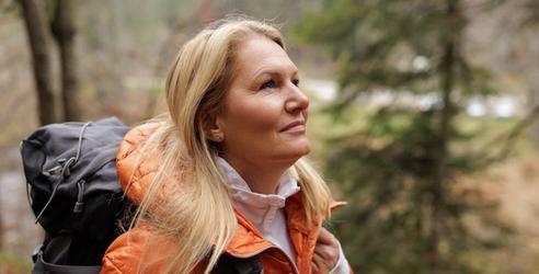 En kvinna med orange jacka och ryggsäck på tur i skogen. foto.