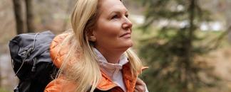 En kvinna med orange jacka och ryggsäck på tur i skogen. foto.