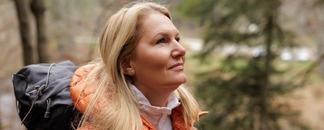 En kvinna med orange jacka och ryggsäck på tur i skogen. foto.