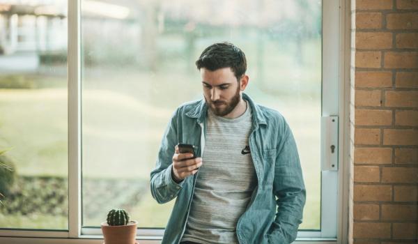 Standing man reading on phone in front of a window. picture.