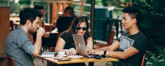 Tre vänner på cafe med macbook och mobiler