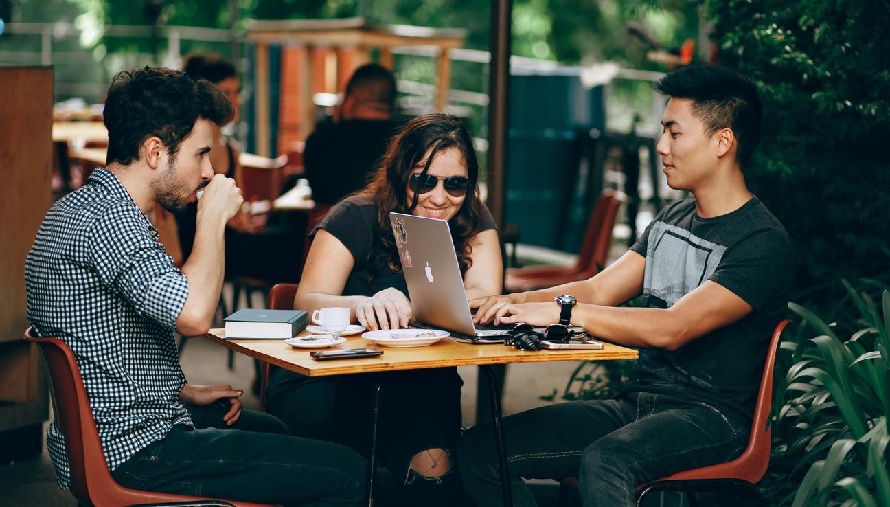 Tre vänner på cafe med macbook och mobiler