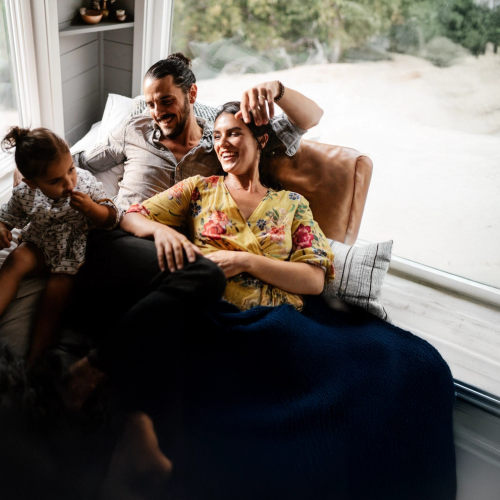 En liten familie koser seg i sofaen. Mammaen og pappaen ser på babyen og smiler. bilde.
