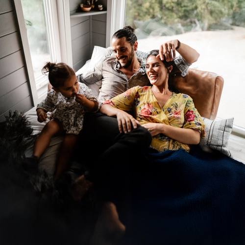 En liten familie koser seg i sofaen. Mammaen og pappaen ser på babyen og smiler. bilde.
