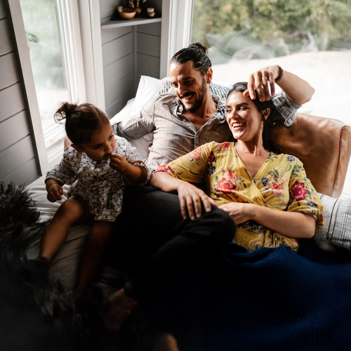 En liten familie koser seg i sofaen. Mammaen og pappaen ser på babyen og smiler. bilde.