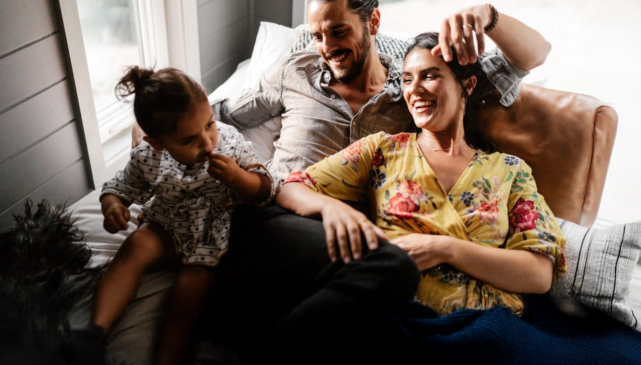 En liten familie koser seg i sofaen. Mammaen og pappaen ser på babyen og smiler. bilde.