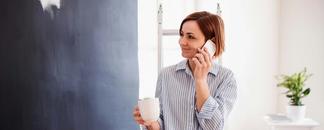 Dame tar en pause fra malinga av vegg. Hun prater i telefon og har en kaffekopp i hånden. bilde.