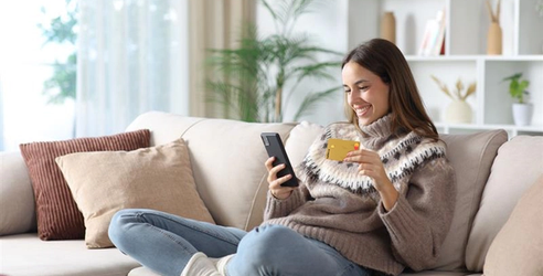 En kvinna sitter i soffan med mobiltelefon och kreditkort. foto.