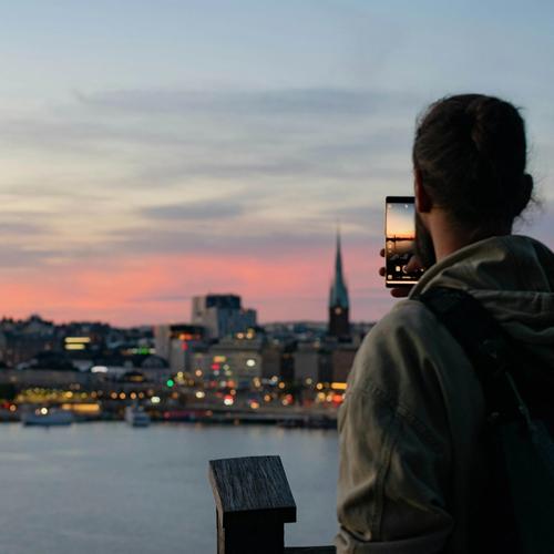 En man tar bild på Stockholms siluett i skymning