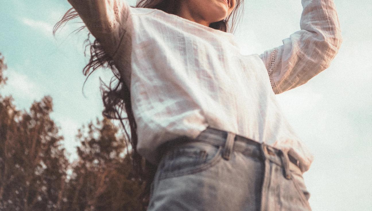 A girl is standing with her arms above her hand like she is dancing.