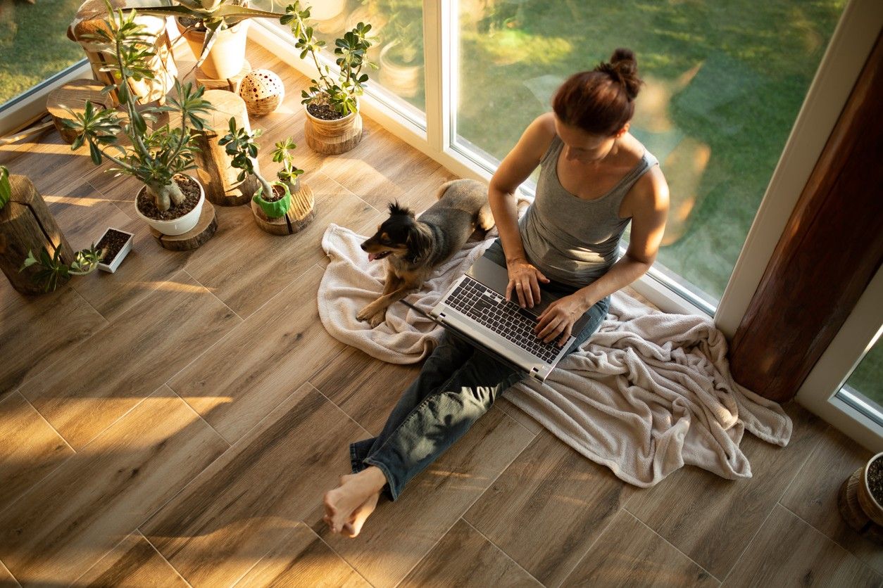 Woman sitting on the floor with laptop on her knee and a dog beside her. picture.