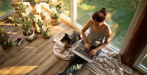 Woman sitting on the floor with laptop on her knee and a dog beside her. picture.