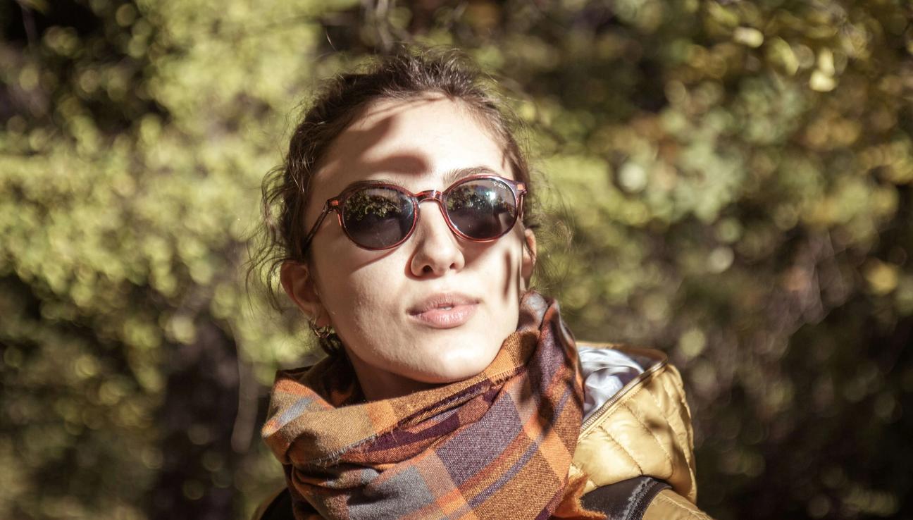 Kvinna med solglasögon och sjal ser mot solen
