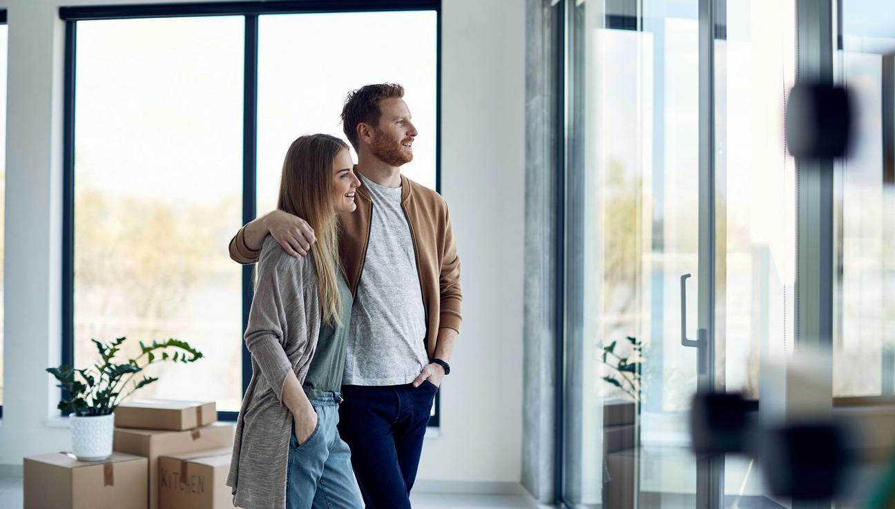 Et par står i den nye boligen sin og ser ut av vinduet. bilde.