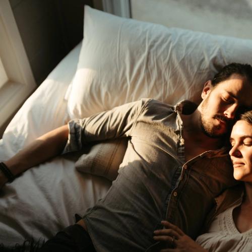 Ett par ligger på sängen och solen lyser in på dem