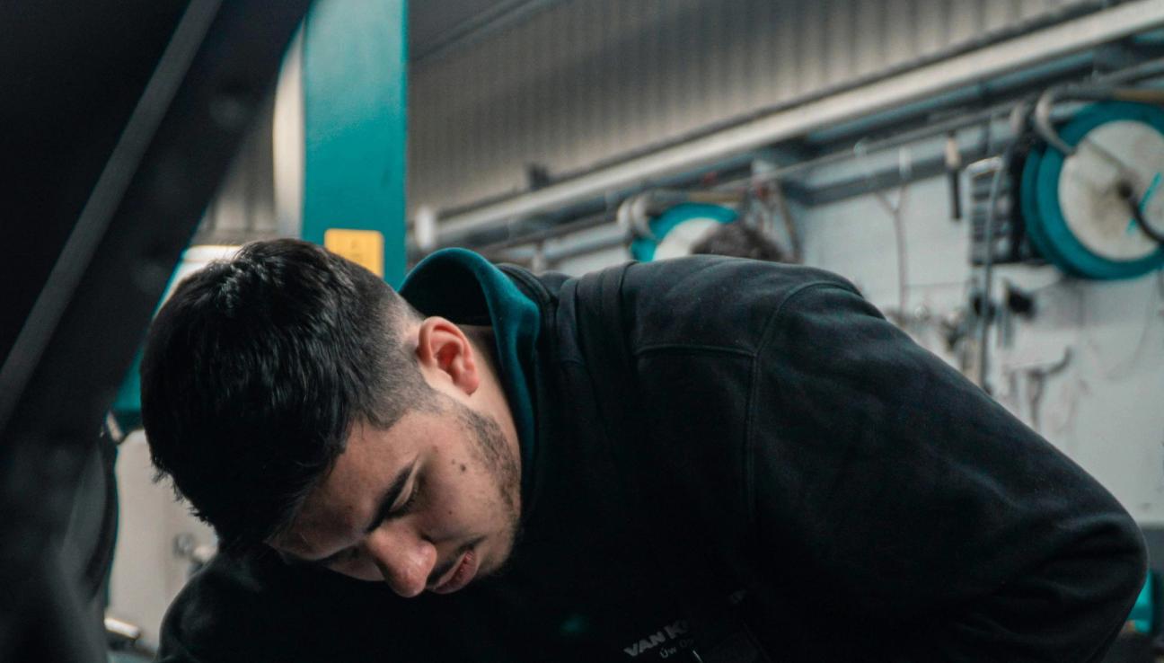 En mekaniker lener seg over en bilmotor inne i et verksted. bilde.