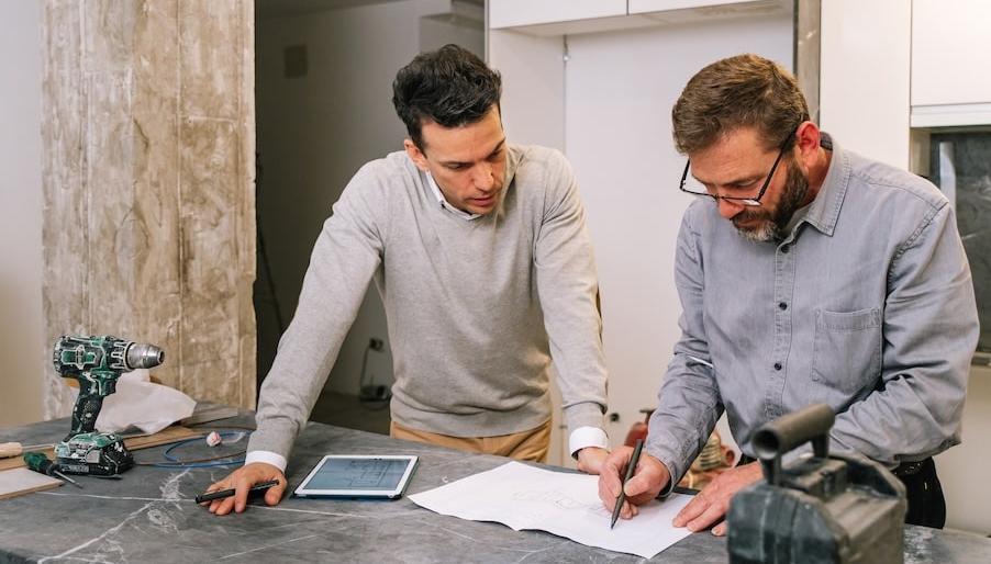 Två män står i ett hus som renoveras och ser på ritningar