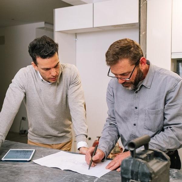 Två män står i ett hus som renoveras och ser på ritningar