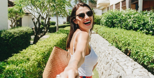 En kvinna på semesterort ler och sträcker handen mot kameran