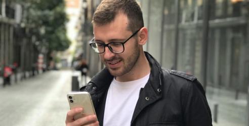 Mann med briller og svart jakke står på fortauet og leser på sin mobil. bilde.