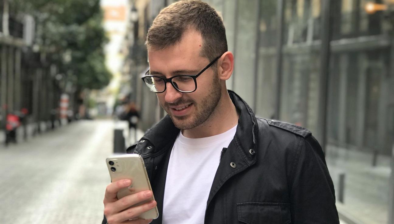 Mann med briller og svart jakke står på fortauet og leser på sin mobil. bilde.