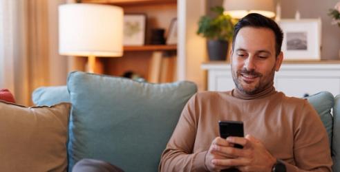 En man sitter i soffan och nätsurfar på telefonen. foto.