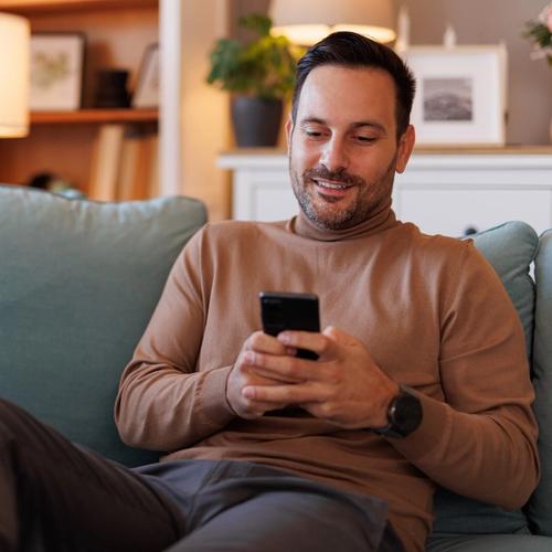En man sitter i soffan och nätsurfar på telefonen. foto.