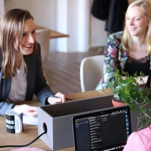 Tre damer jobber sammen ved et bord. Det står blomster, kaffekopp og pc foran dem. bilde.