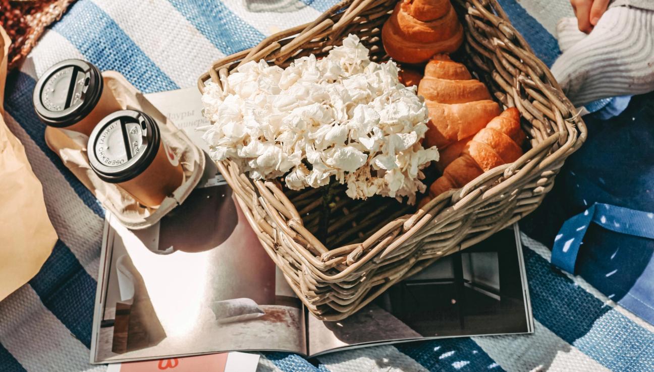 En picknickkorg fylld med croissanter och blommor på en blå och vit randig picknickfilt