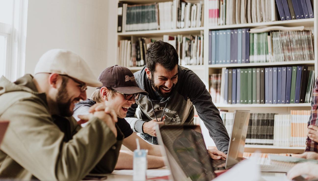 A group of friends is sitting around a computer and laughing.