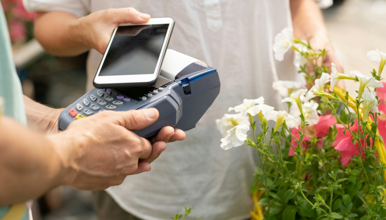 En man kjøper blomster og betaler med kredittkort i mobilen. bilde.