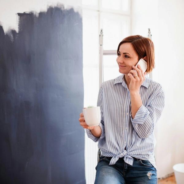 Nainen pitää taukoa remontin keskellä, puhuu puhelimeen ja juo kahvia. Valokuva.