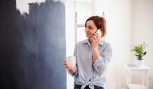 Nainen pitää taukoa remontin keskellä, puhuu puhelimeen ja juo kahvia. Valokuva.