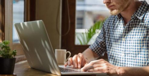 En man sitter vid sin laptop med en kaffekopp vid sidan av. foto.