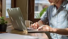 En man sitter vid sin laptop med en kaffekopp vid sidan av. foto.
