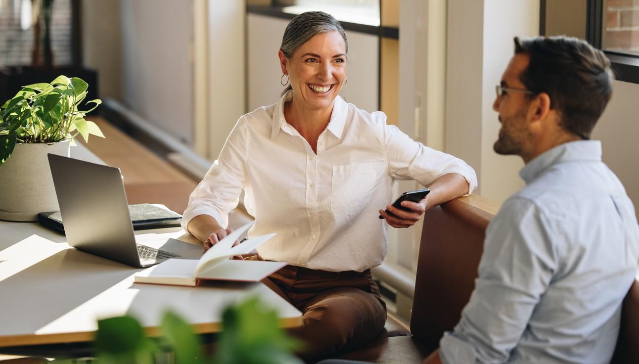 Dame og mann snakker sammen ved skrivebordet. bilde.