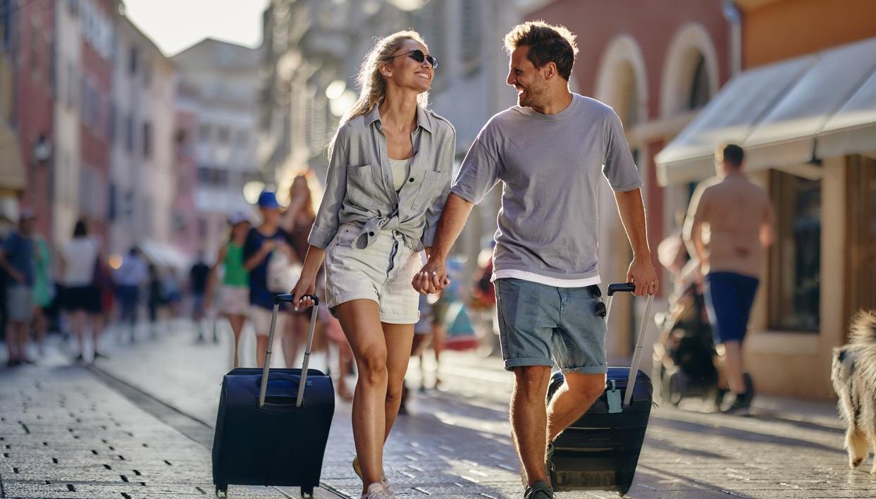 Man och kvinna på semesterresa. De drar en resväska var bakom sig. foto.
