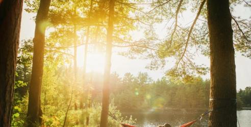 Ett par sitter i en hängmatta vid en sjö. Solen skiner.