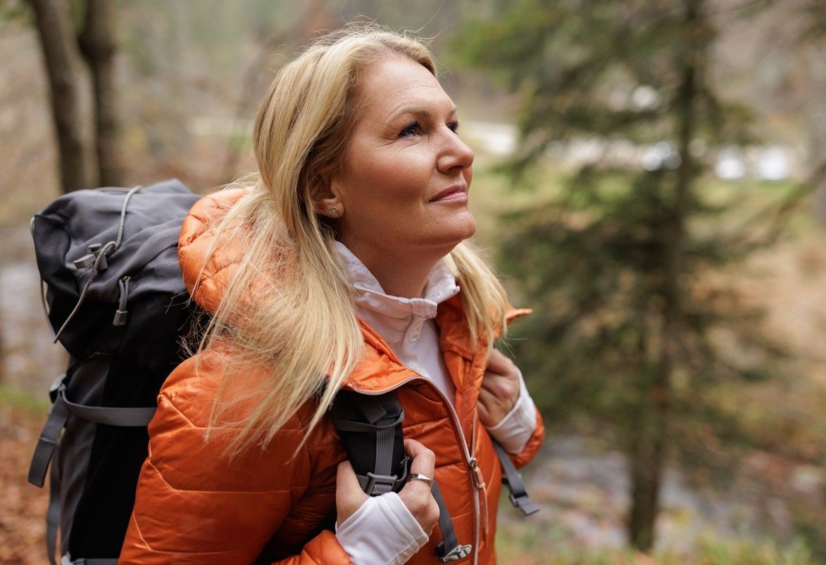 En dame med oransje jakke og sekk på tur i skogen. bilde.