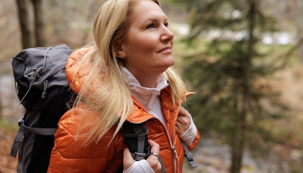 En dame med oransje jakke og sekk på tur i skogen. bilde.