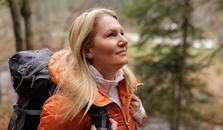 En dame med oransje jakke og sekk på tur i skogen. bilde.